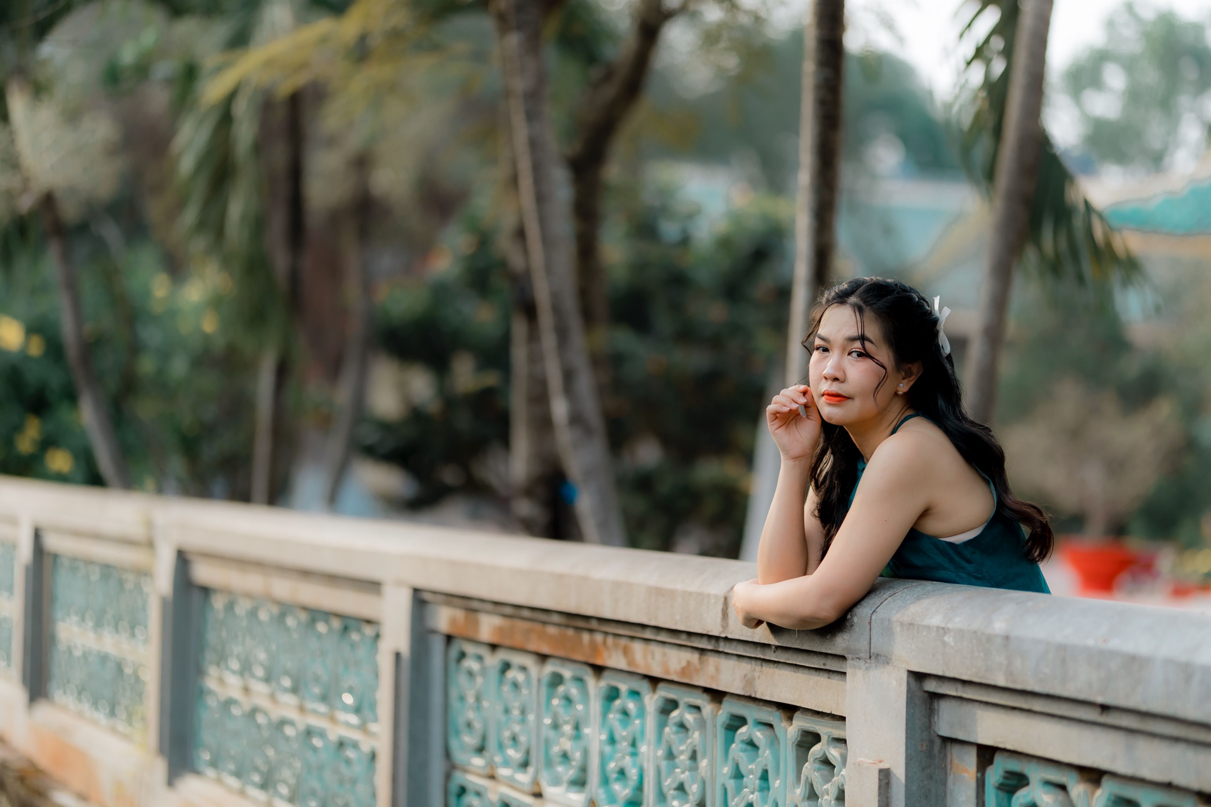 Woman in a peaceful outdoor setting leaning on a decorative bridge, immersed in thought.