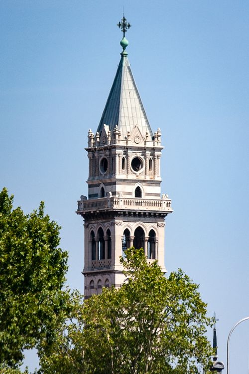 Free View of a historic bell tower surrounded by green trees in Madrid, Spain, under a clear blue sky. Stock Photo