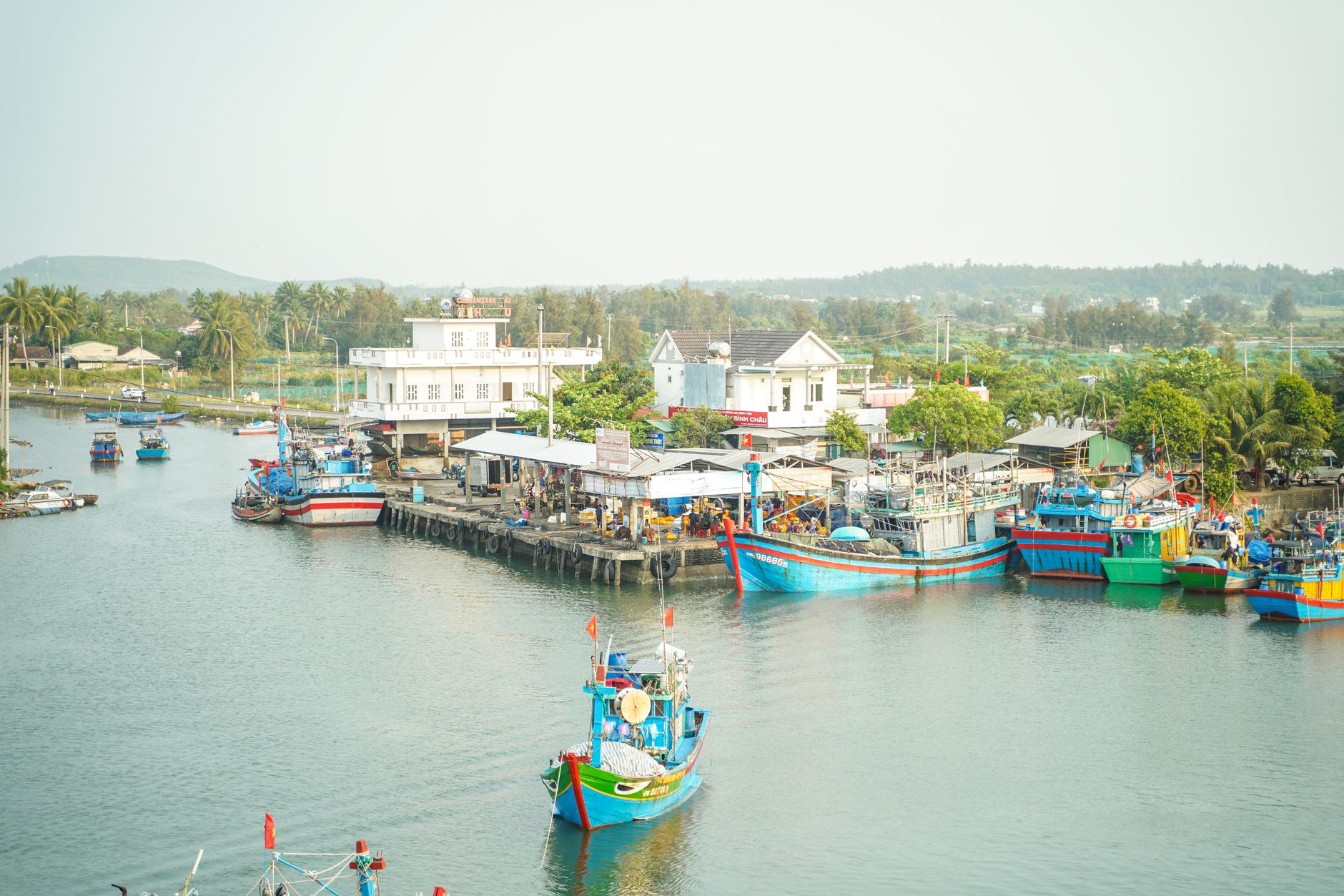 A vibrant scene of colorful fishing boats docked in a serene coastal village with lush surroundings.