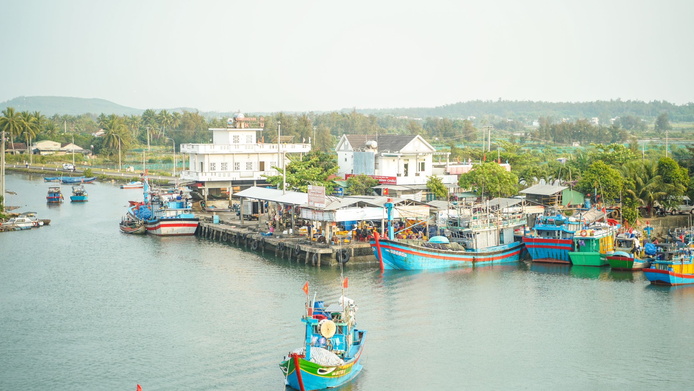 A vibrant scene of colorful fishing boats docked in a serene coastal village with lush surroundings.