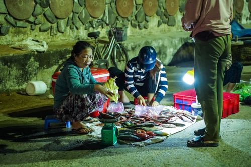 Free Two women selling fresh fish at a night market. Street vendor setup with fresh catch displayed. Stock Photo