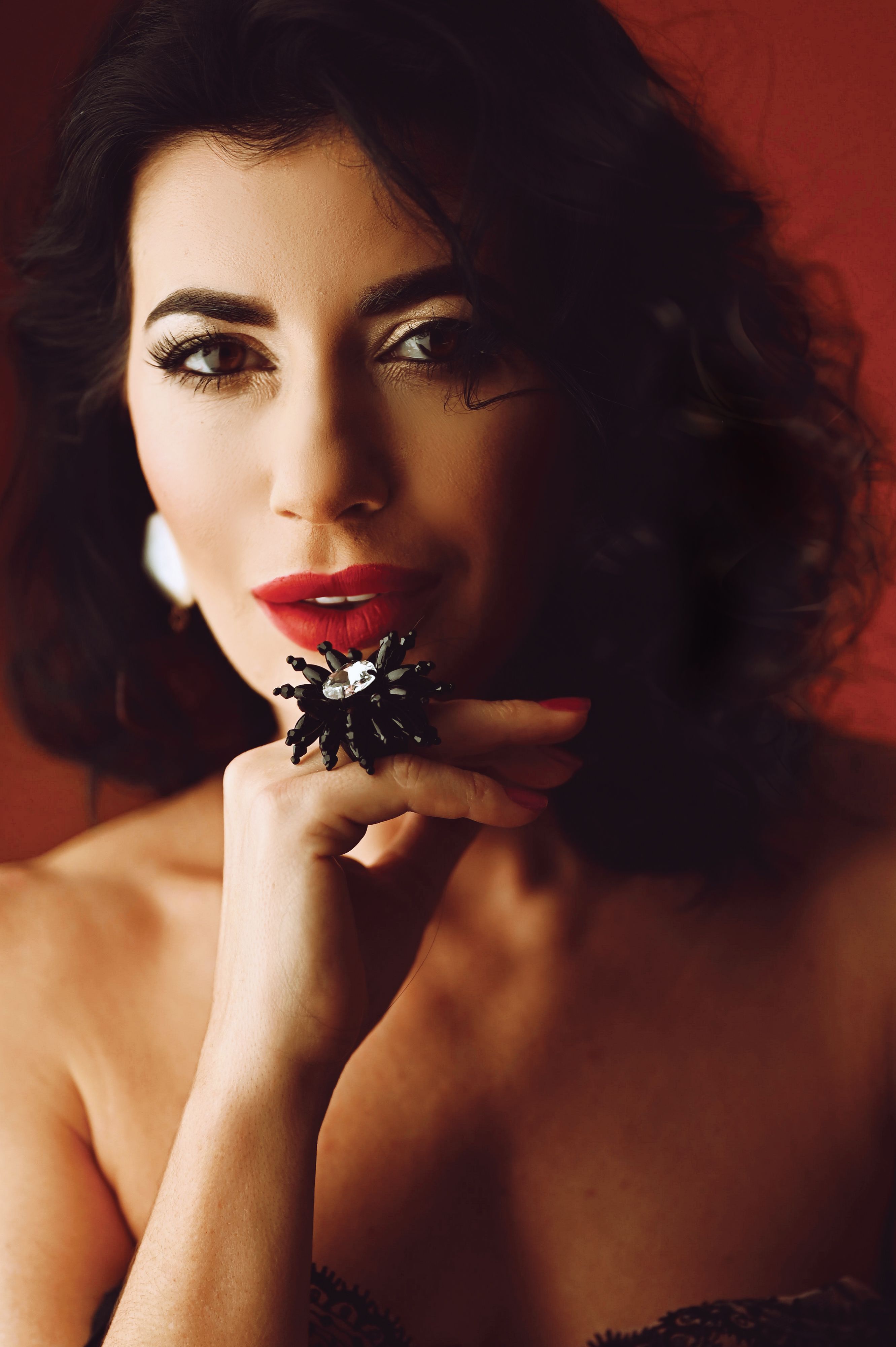 Close-up portrait of an elegant woman with red lips and a black flower ring, exuding sophistication.