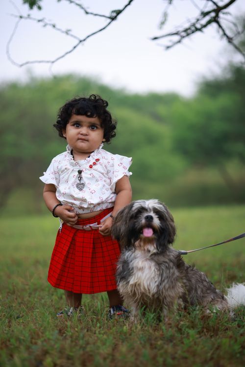 Free A cute baby in red attire with a Shih Tzu dog outdoors in a vibrant green park, capturing a joyful moment. Stock Photo