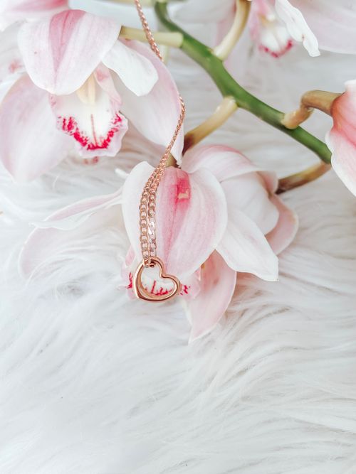 Free A delicate rose gold heart necklace beautifully draped over soft pink orchids on a white furry background. Stock Photo