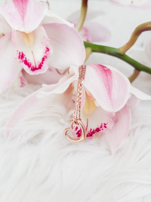 Free A delicate rose gold heart necklace elegantly draped over a vibrant pink orchid flower. Stock Photo
