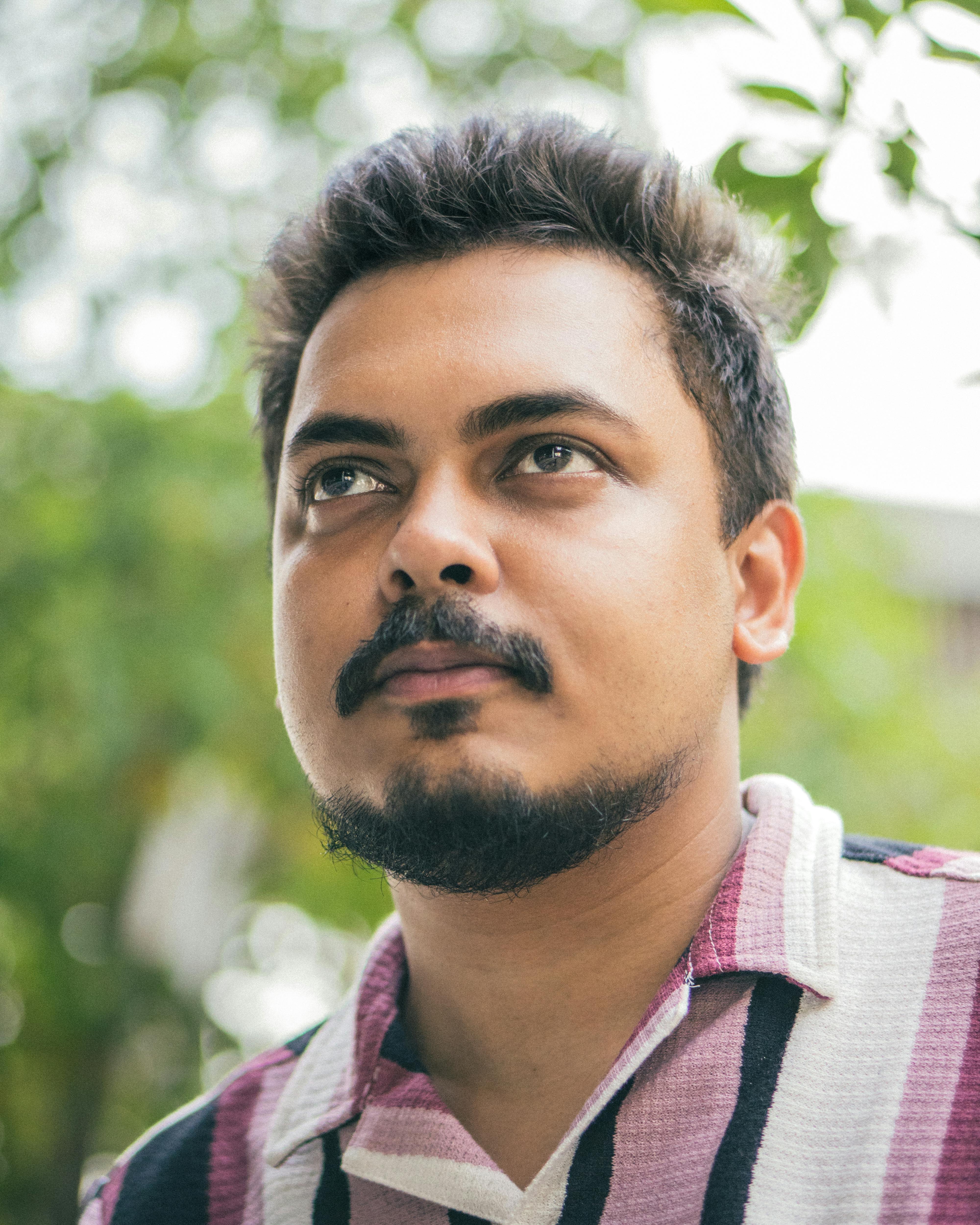 Close-up portrait of a young man looking thoughtful outdoors with greenery in the background.