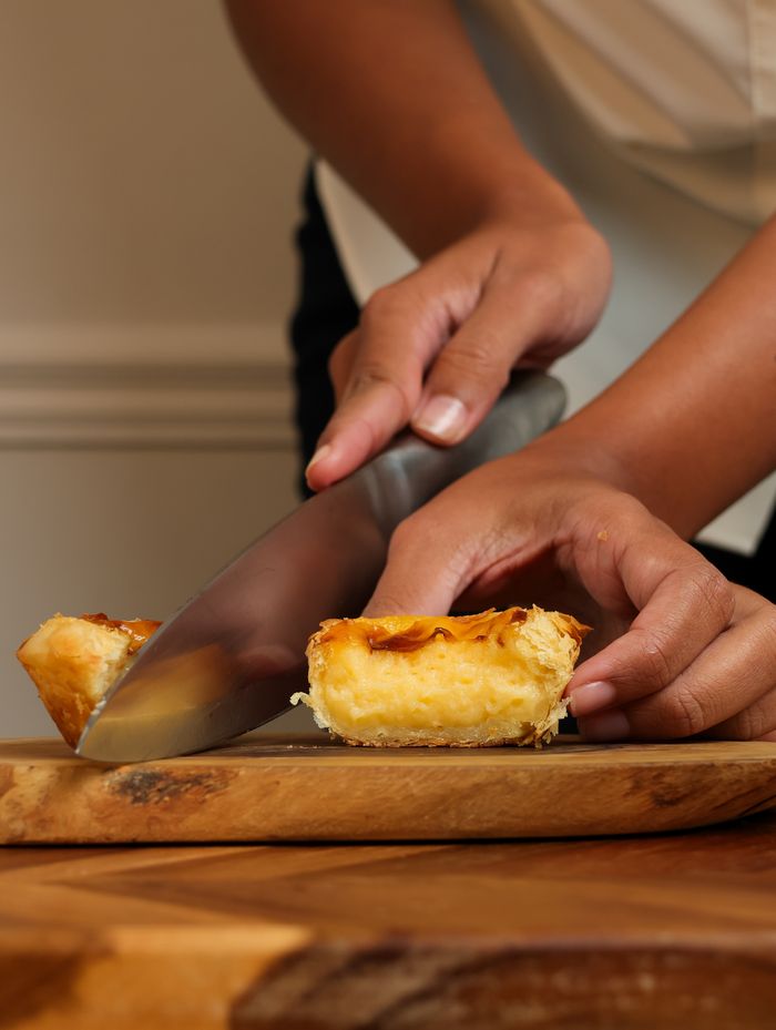 Hands slicing a custard tart on a wooden board