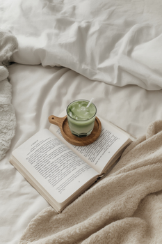 Open book and iced matcha on a cozy bed setting, inviting relaxation.