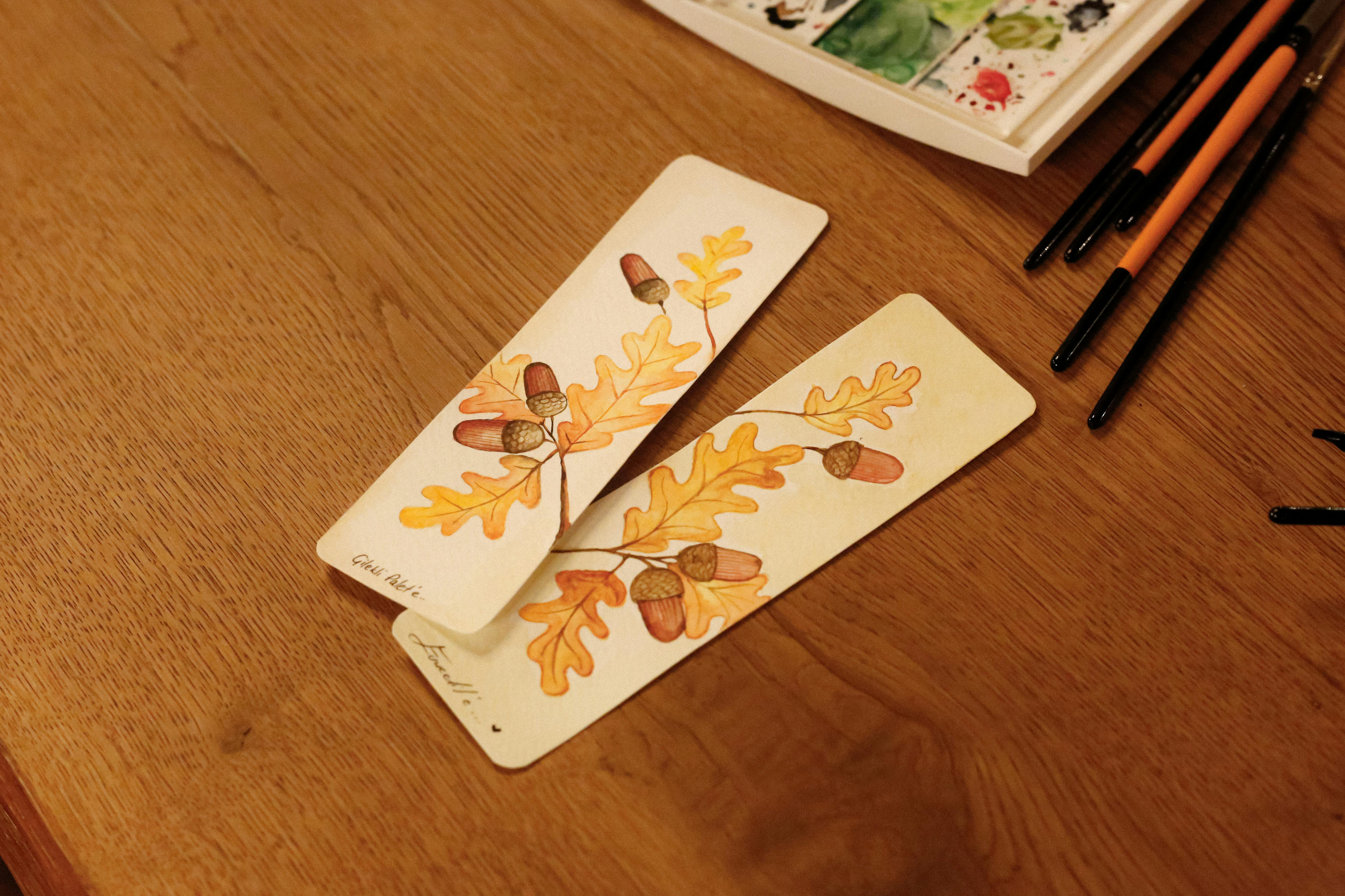 De franc Punts de llibre de fulles de roure pintats a mà sobre una taula de fusta envoltada de materials d'art. Foto d'estoc