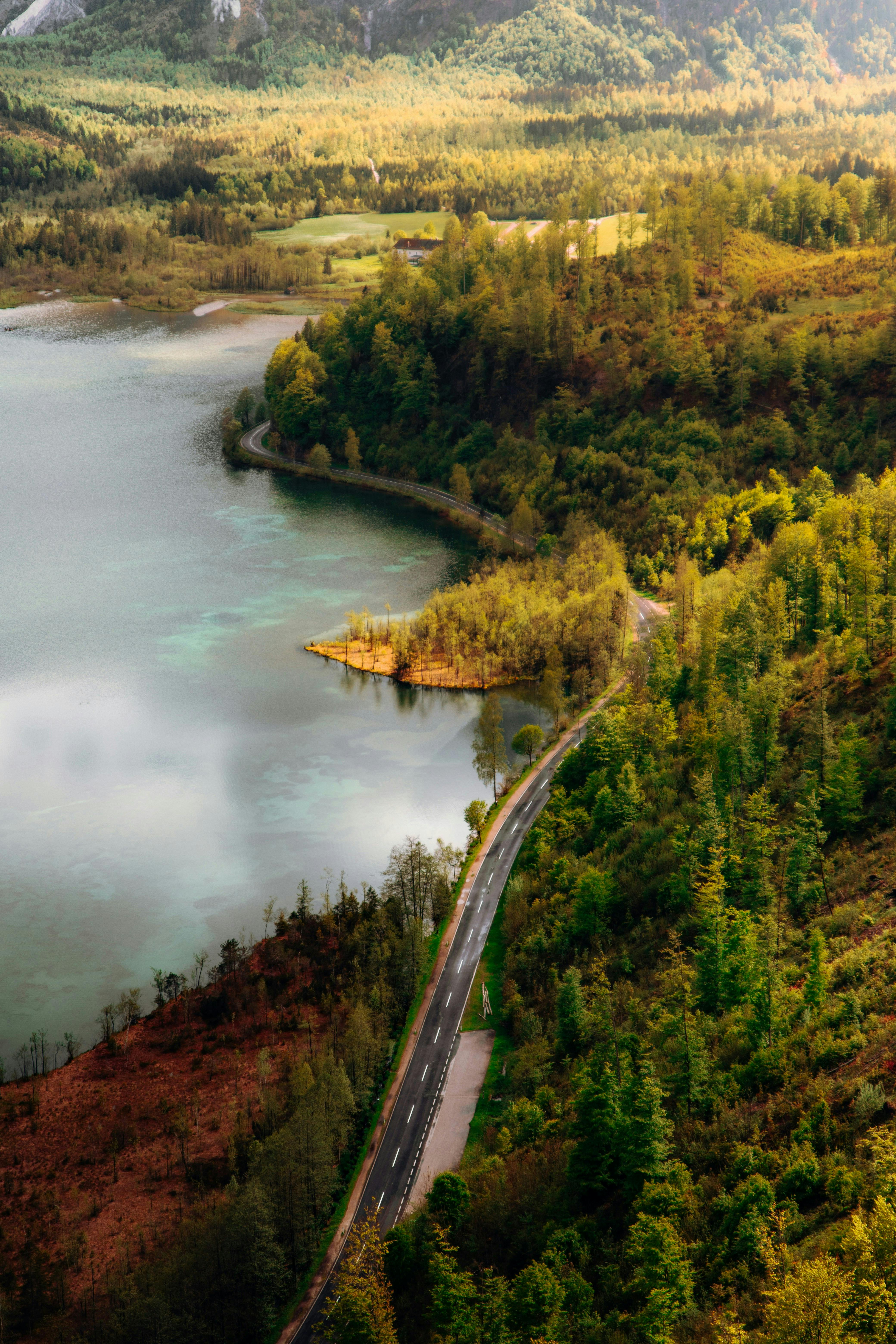 Aerial view of winding road along a vibrant alpine lake in Austria's mountains.