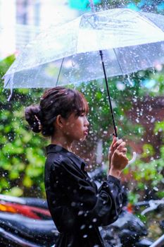 A young woman stands under an umbrella during a rainy day in Hue, Vietnam.