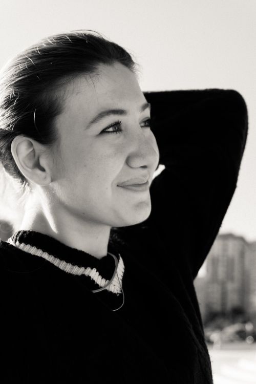 Free Monochrome portrait of a young woman smiling outdoors with buildings in the background. Stock Photo