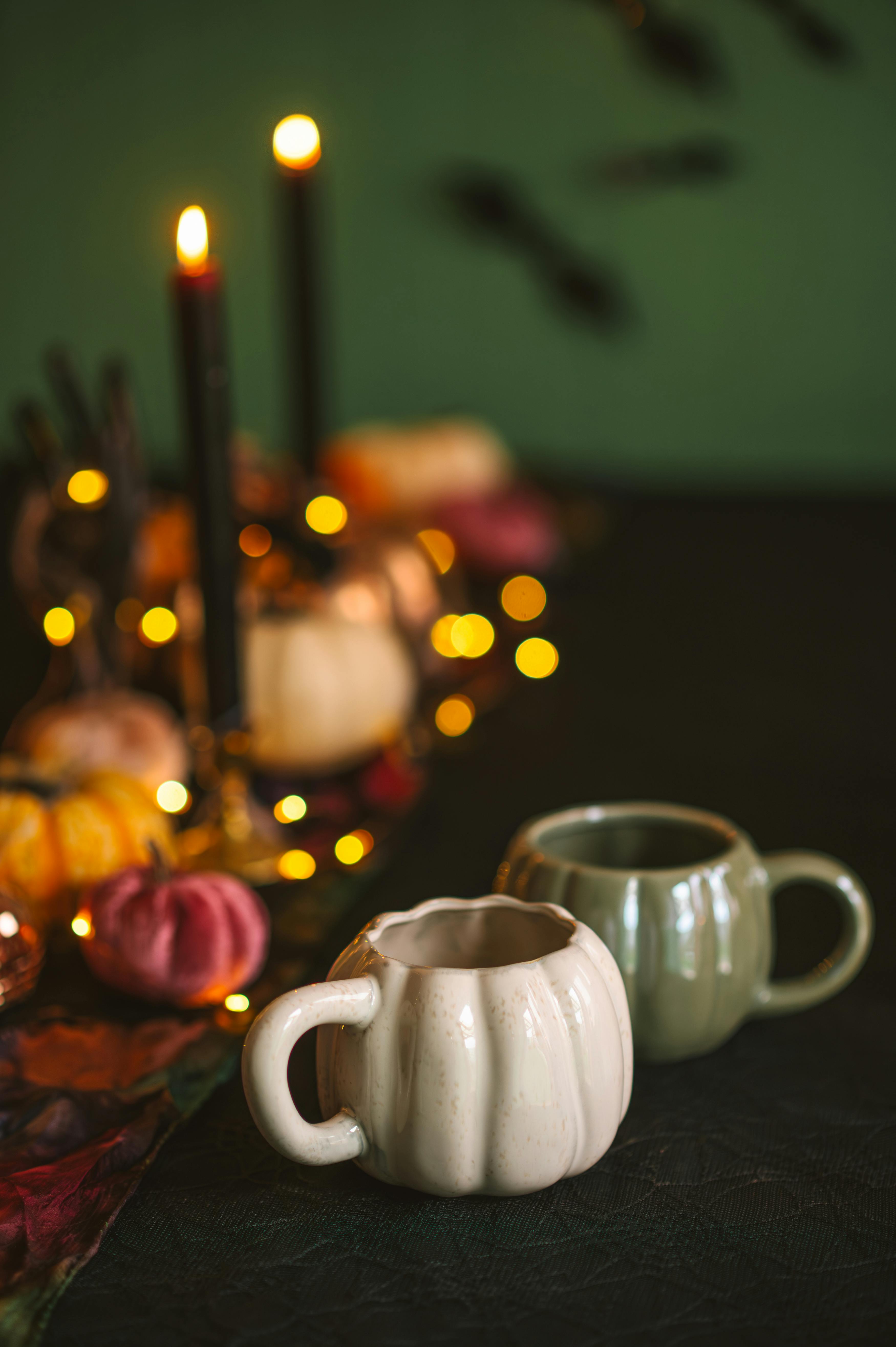 Warm autumn table decor with pumpkin-shaped mugs, candles, and fall leaves.