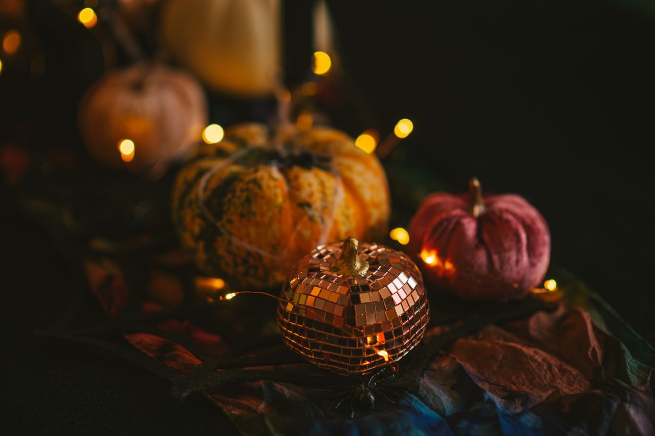 Disco-ball mosaic pumpkin with velvet pumpkins and fairy lights on a dark table