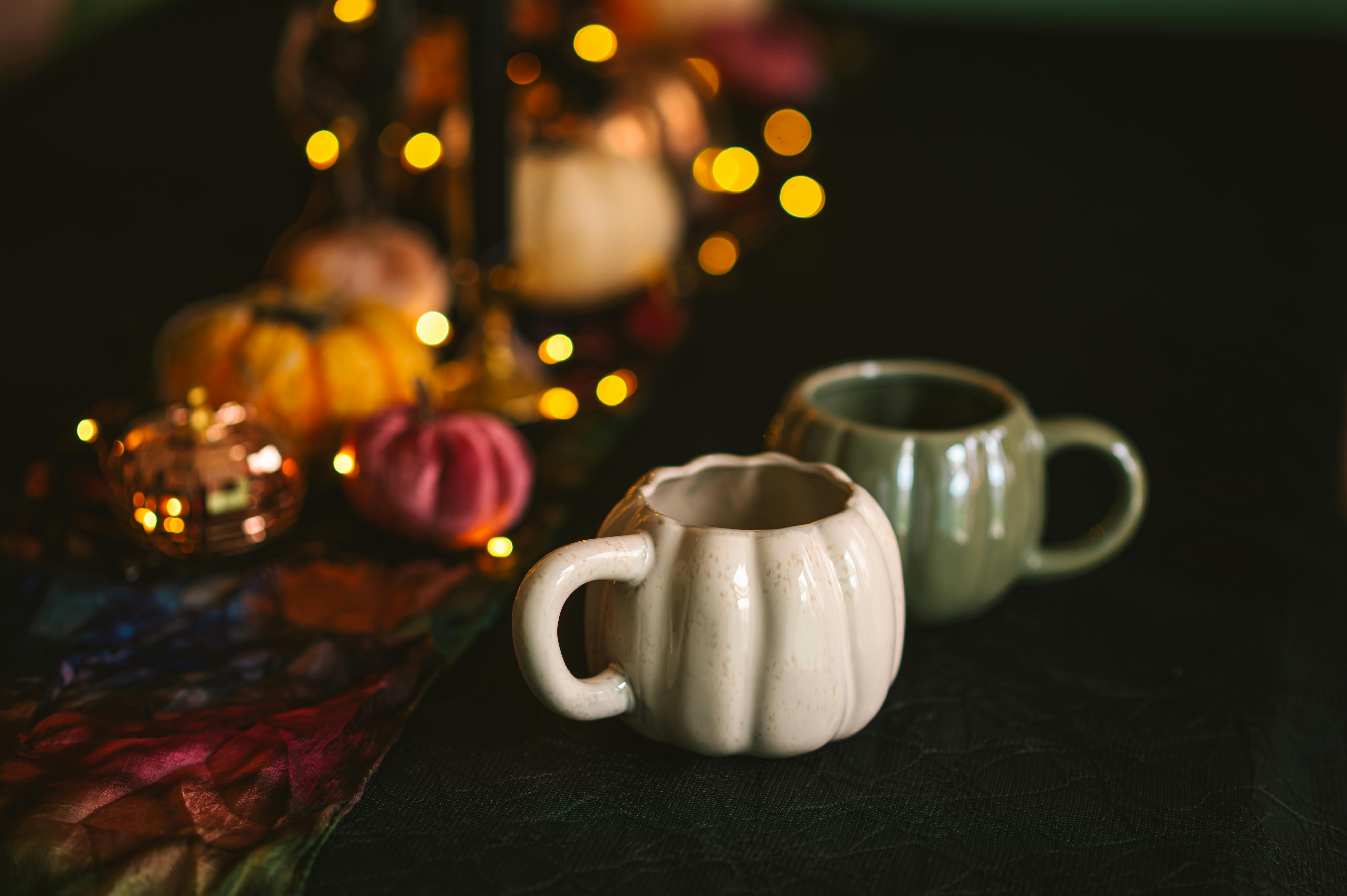 A warm autumn table decor featuring pumpkin-shaped mugs and vibrant lights.