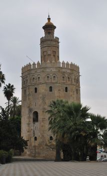 Historic Torre del Oro tower in Seville, Spain, surrounded by palm trees.