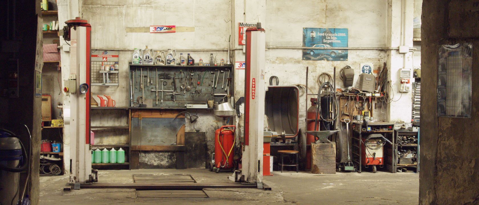 An empty, rustic car workshop featuring tools, machinery, and car lifts in an industrial setting.