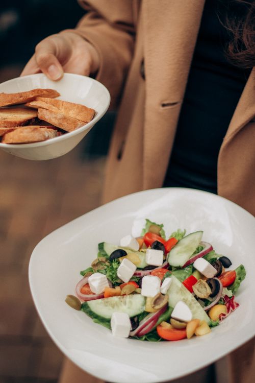 Free A person holds a fresh vegetable salad and crispy bread slices outdoors. Stock Photo