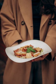 Close-up of a woman holding a Caesar salad garnished with basil outdoors.
