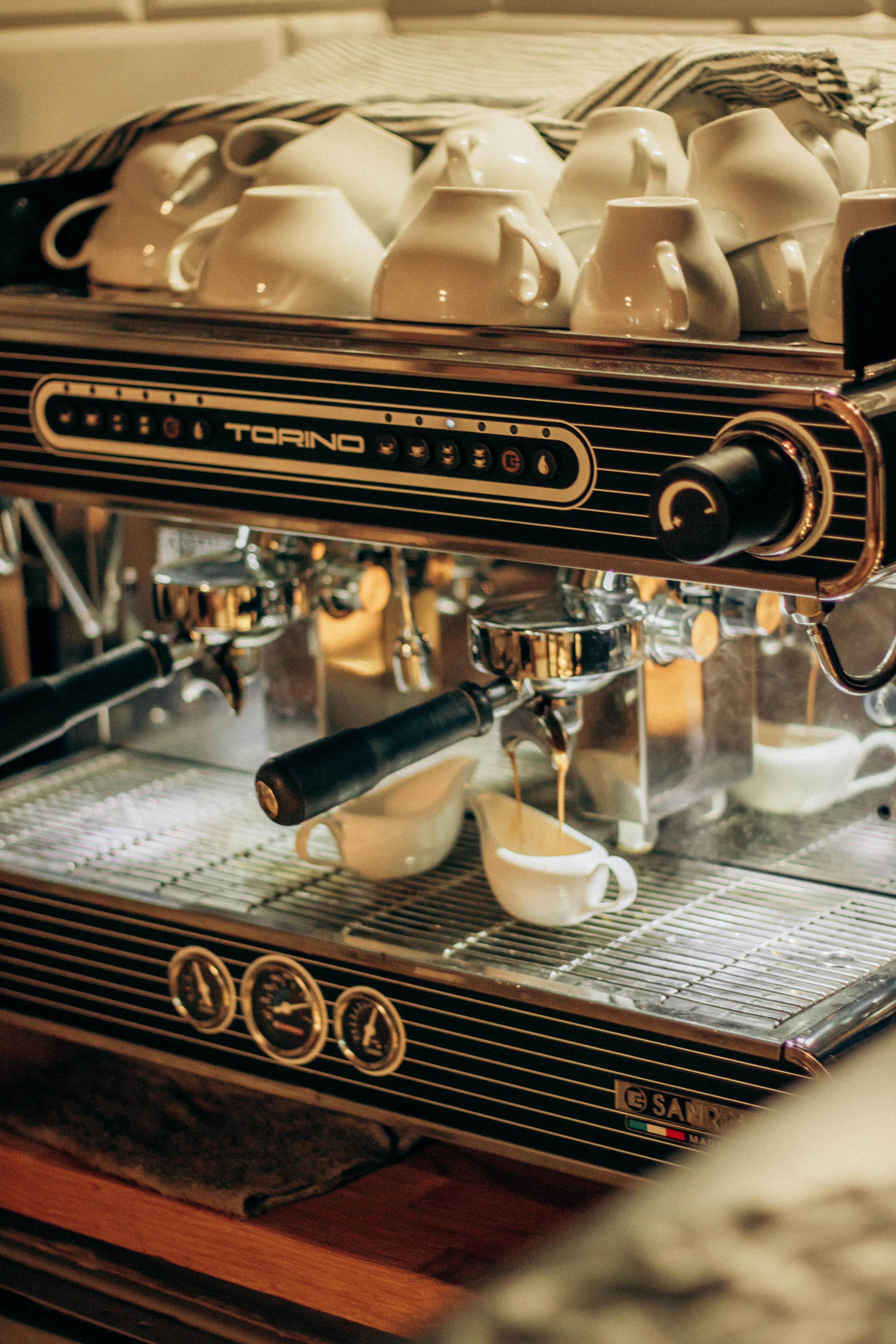 Close-up of a professional espresso machine brewing coffee into cups with more cups on top.
