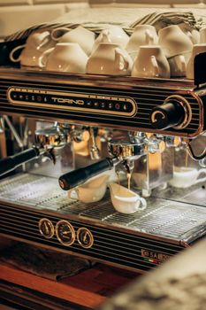 Close-up of a professional espresso machine brewing coffee into cups with more cups on top.