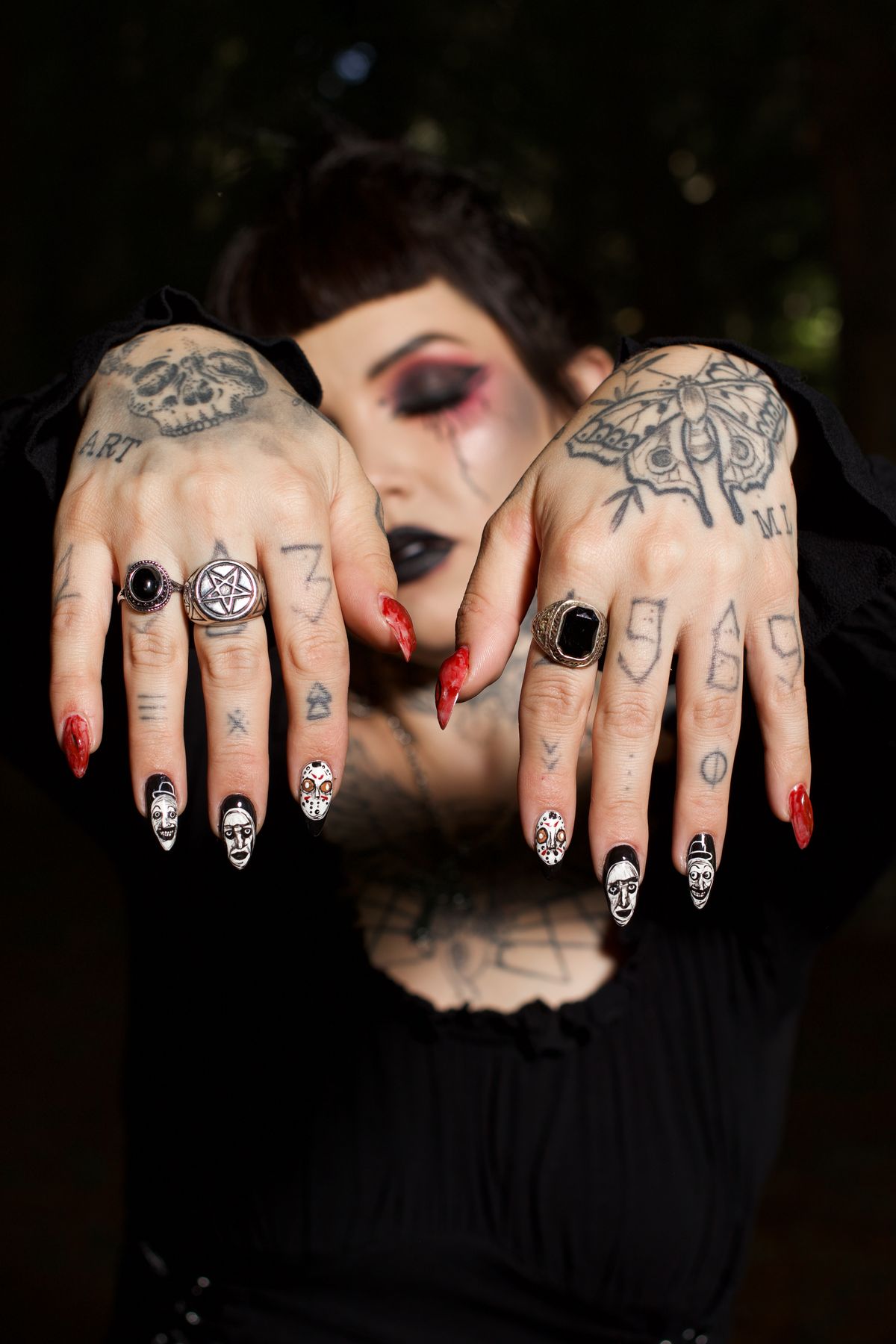 Gothic woman displaying intricate tattoos and nail art with rings.