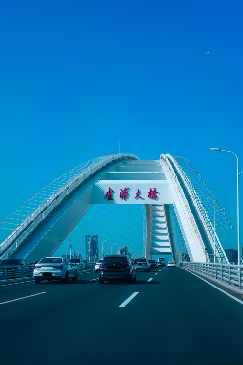 Free Cars driving on a modern arch bridge under a clear blue sky. Vibrant and dynamic urban scene. Stock Photo