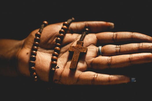 A detailed view of a hand holding a wooden rosary and cross, symbolizing faith.