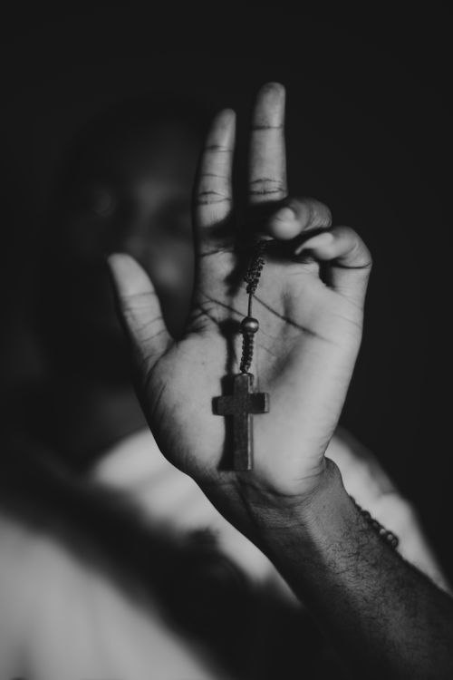 Free Monochrome image of an outstretched hand holding a rosary with a cross in focus, symbolizing faith and spirituality. Stock Photo