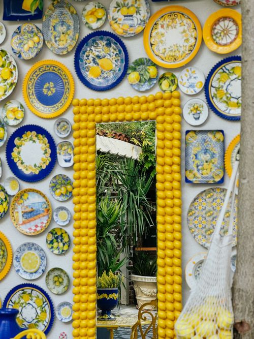 Free A colorful display of ceramic plates and lemons surrounding a mirror, reflecting a garden. Stock Photo