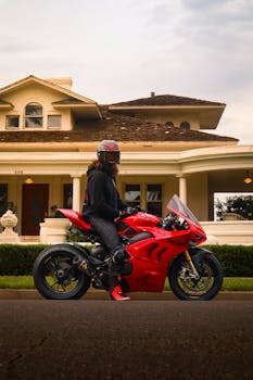 Motorcyclist on red sports bike parked in front of a classic suburban house.