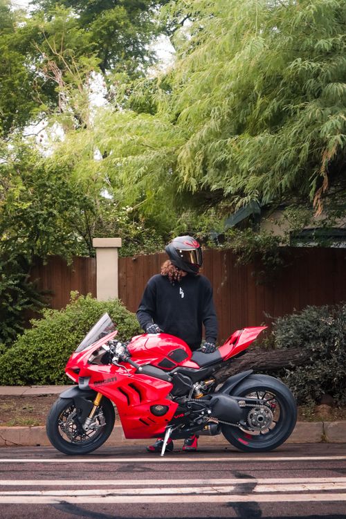 Free Man in helmet with red sports bike on tree-lined street. Stock Photo