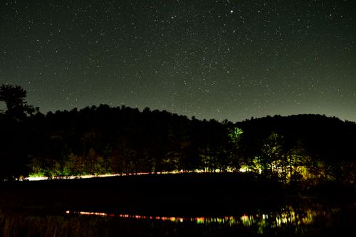 Free Night sky filled with stars above a forest near Blairsville, Georgia, showcasing car light trails and reflections. Stock Photo
