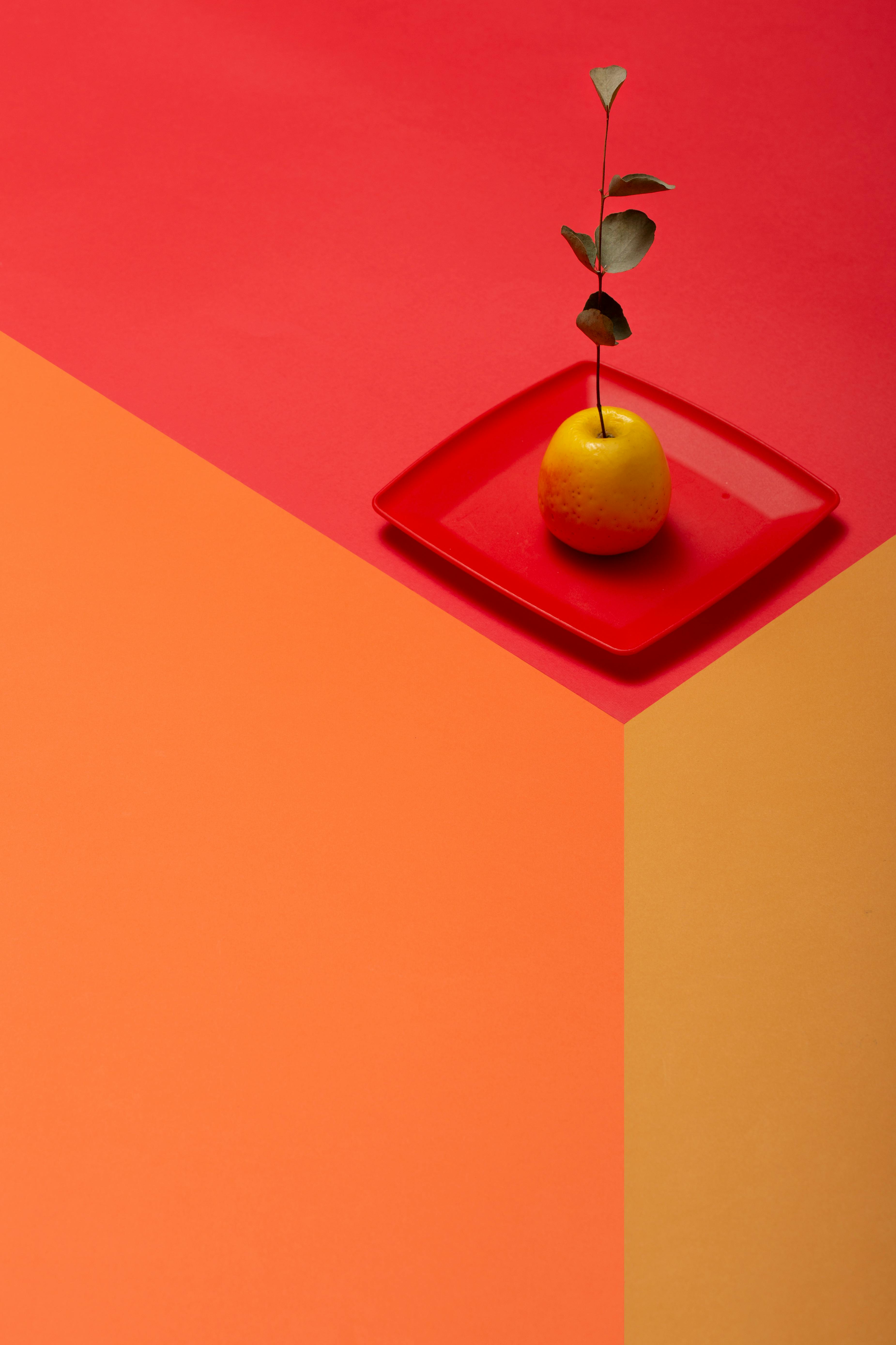 Gratis Apel kuning cerah di atas piring merah dengan latar belakang geometris berwarna-warni. Foto Stok