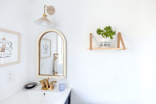 Bright and simple bathroom interior with a gold-framed mirror and decorative shelf.