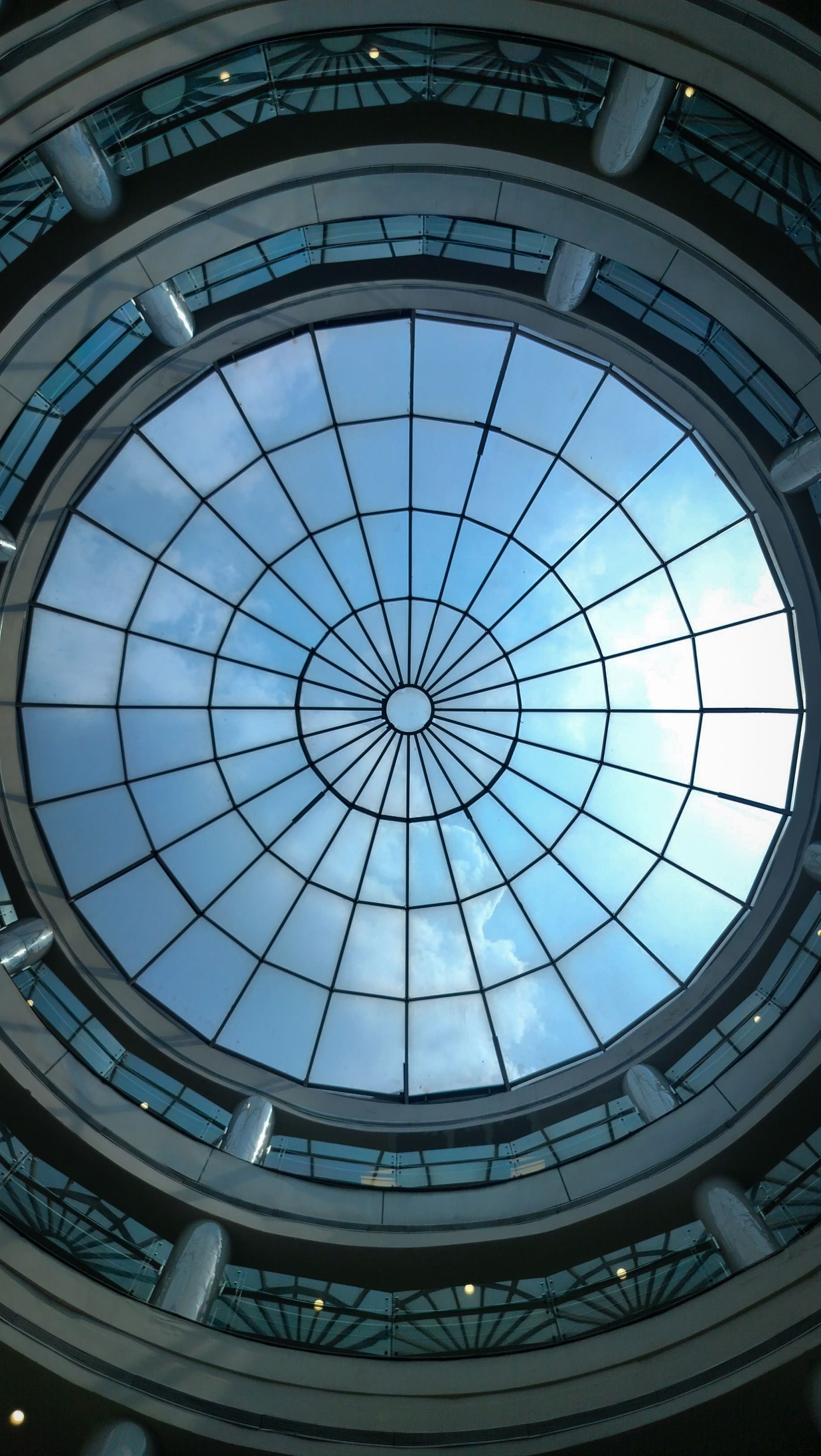 Elegant circular dome with a glass ceiling showcasing blue sky and white clouds.