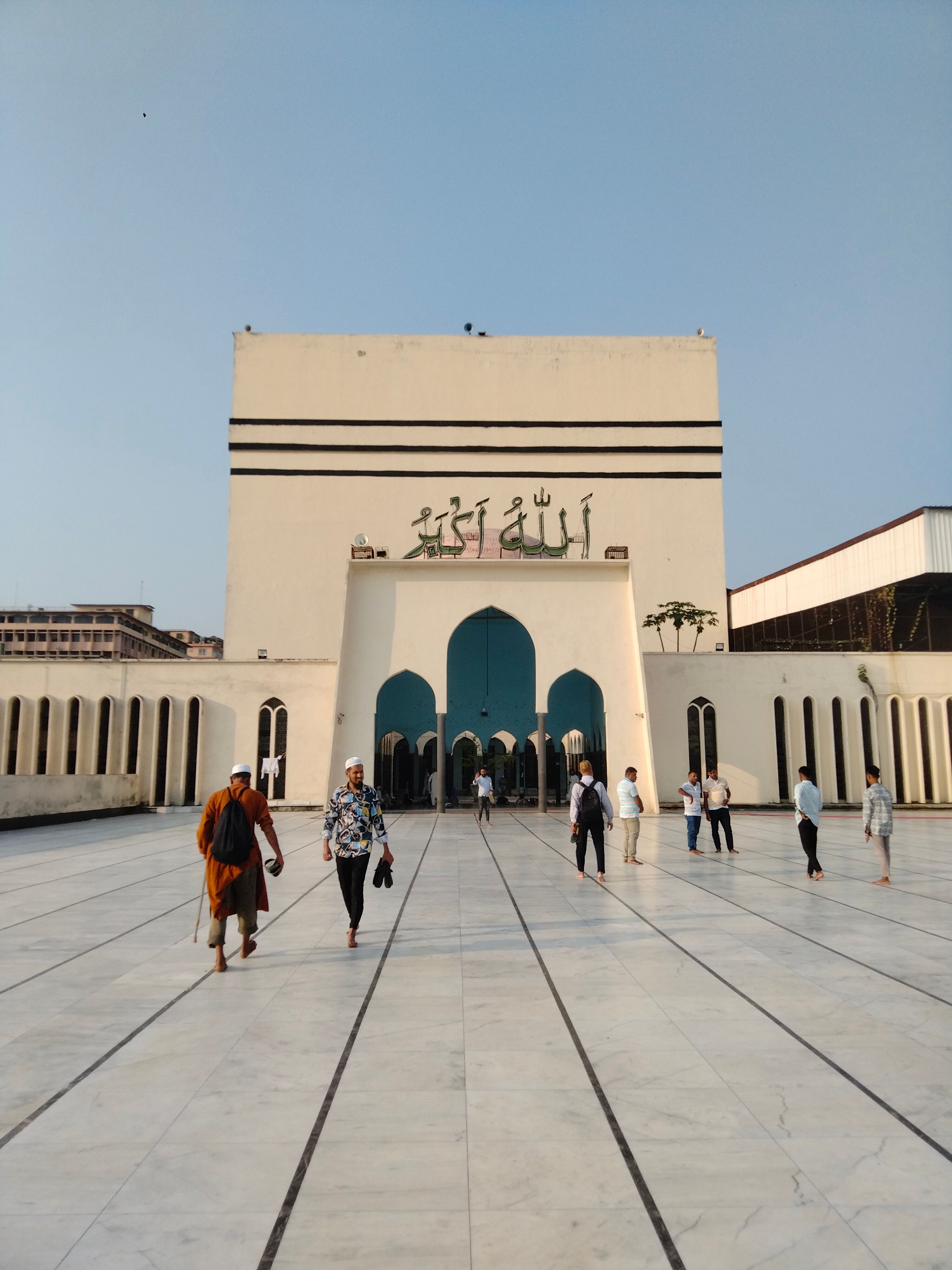 People walking towards a mosque entrance under clear skies, showcasing modern Islamic architecture.