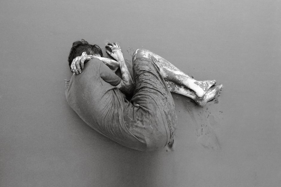 Fotomural Fotografía artística en blanco y negro de una persona cubierta de barro en posición fetal.