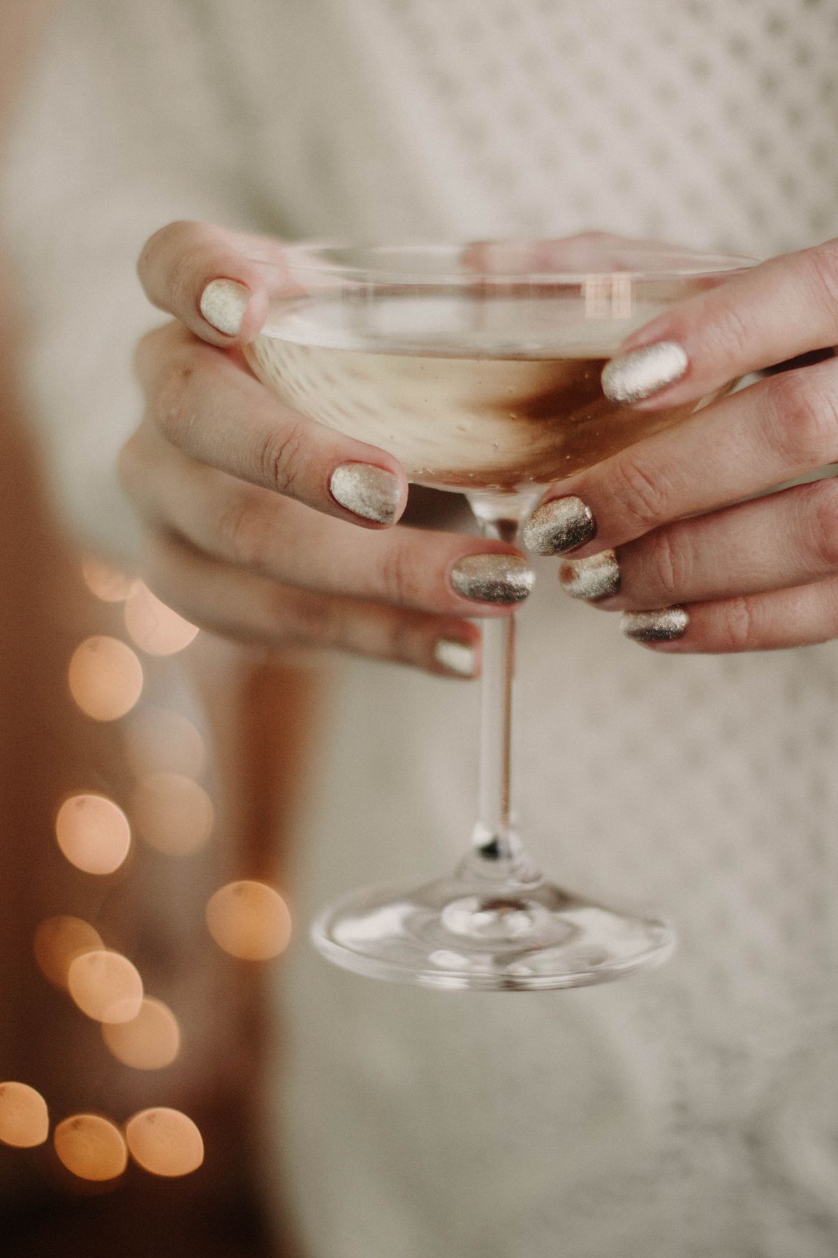 Close-up of hands holding a sparkling wine glass with bokeh lights, perfect for holiday or event themes.