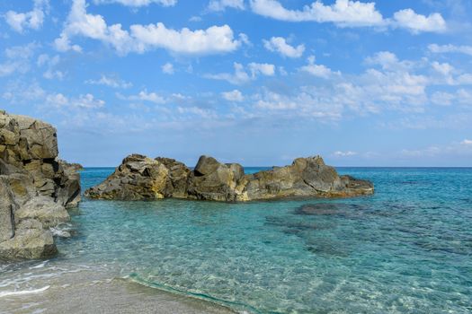 A tranquil beach scene featuring clear blue waters and rocky formations under a bright blue sky.