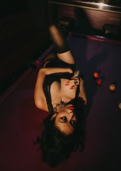Artistic portrait of a woman in seductive pose on a billiards table.