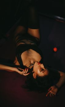 Artistic pose of a woman in lingerie on a billiard table, moody lighting.