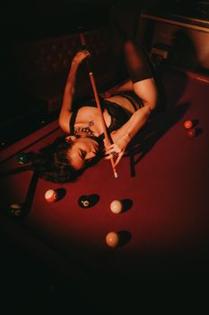 A woman in lingerie poses seductively on a pool table in low light.