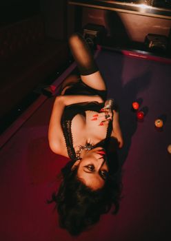 A fashionable woman posing on a pool table with alluring lighting and shadows.