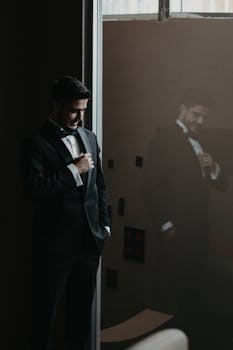 Man in formal tuxedo reflected in glass, creating a dramatic and stylish look.