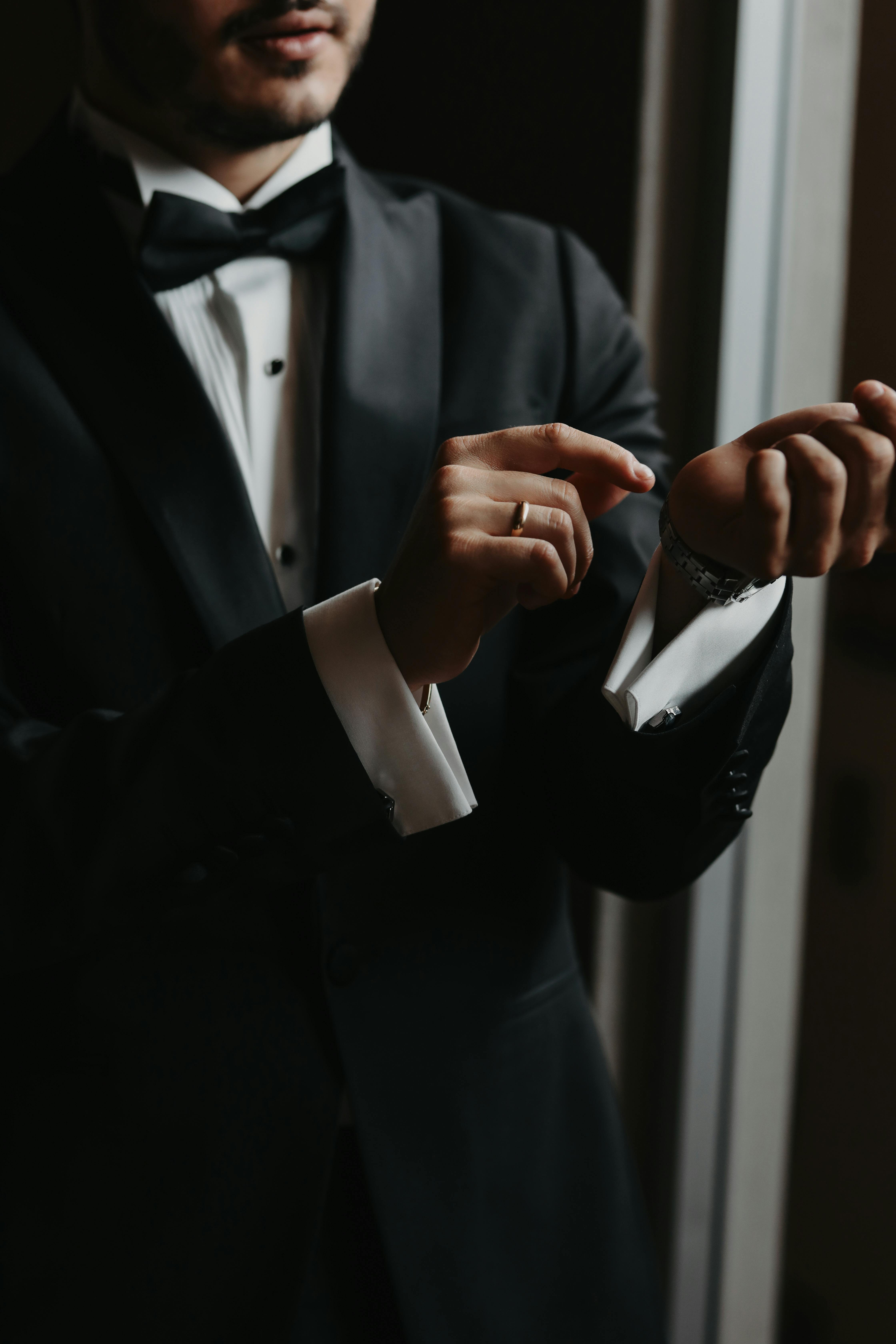 Gratis Un uomo in smoking nero che sistema i gemelli, sottolineando eleganza e stile. Foto a disposizione