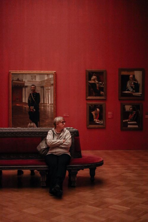 Free A woman sits on a bench in an art gallery, contemplating various portraits on the walls. Stock Photo