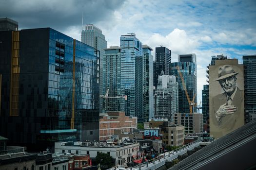 Skyline view of Downtown Montreal featuring a notable mural of an iconic figure, with modern skyscrapers under a cloudy sky.