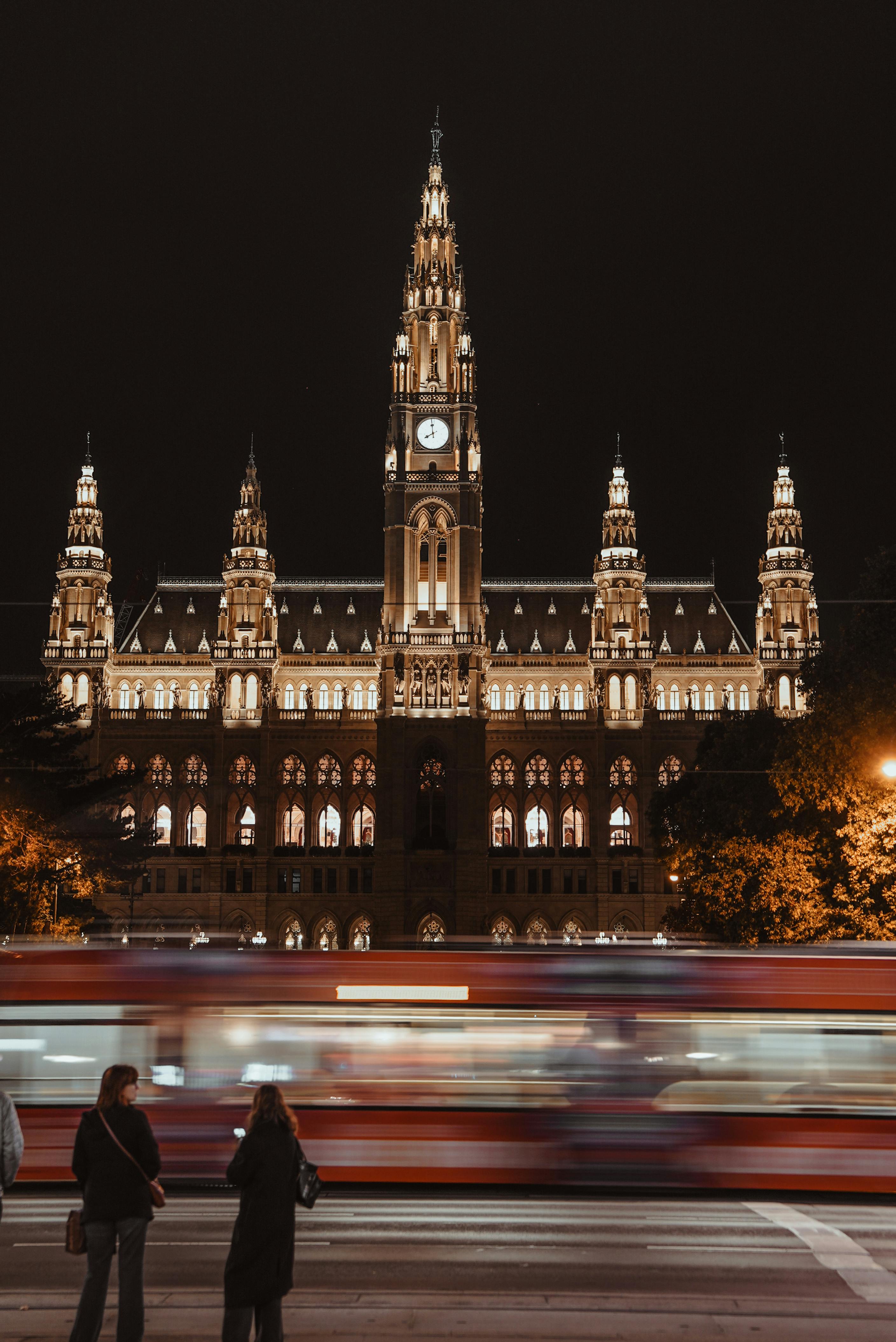 Long exposure capturing Vienna City Hall at night with blurred tram motion creating a dynamic urban scene.
