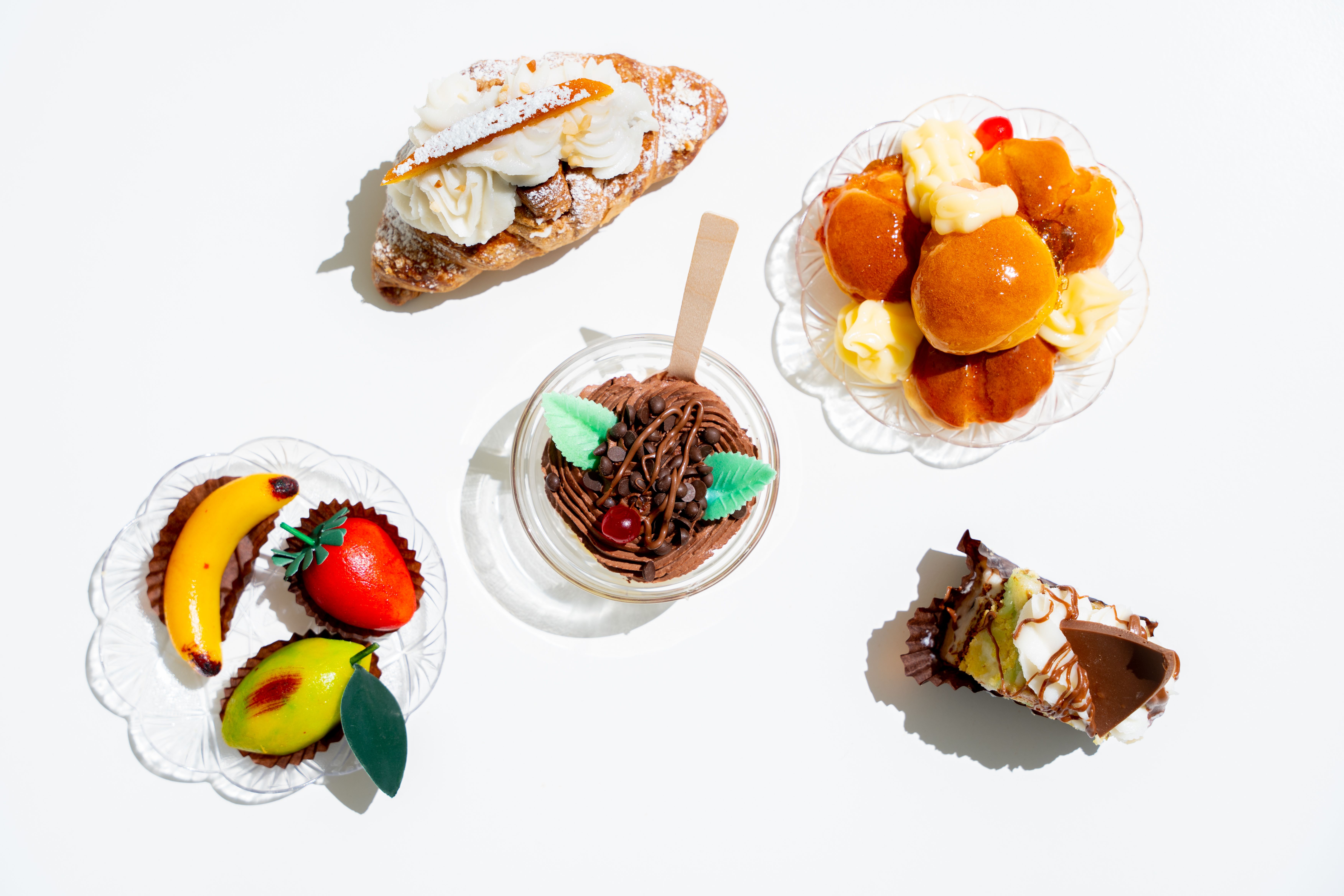 A flat lay of various gourmet pastries including chocolate mousse, cream puff, and fruit tart.